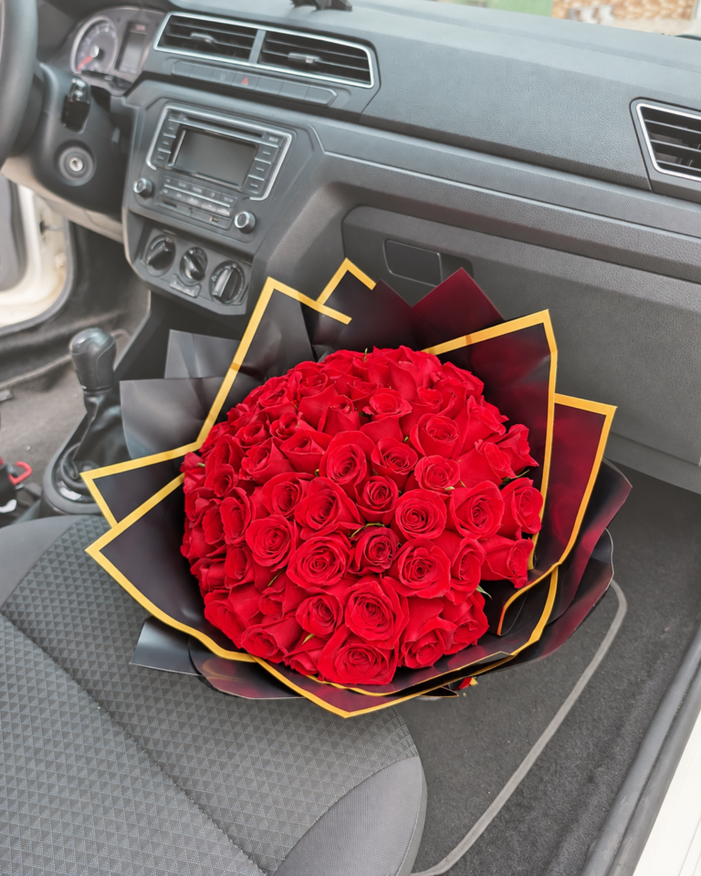 Bouquet de 48 rosas rojas en papel coreano rosado dentro de un vehículo, con retoque crema suave en el entorno