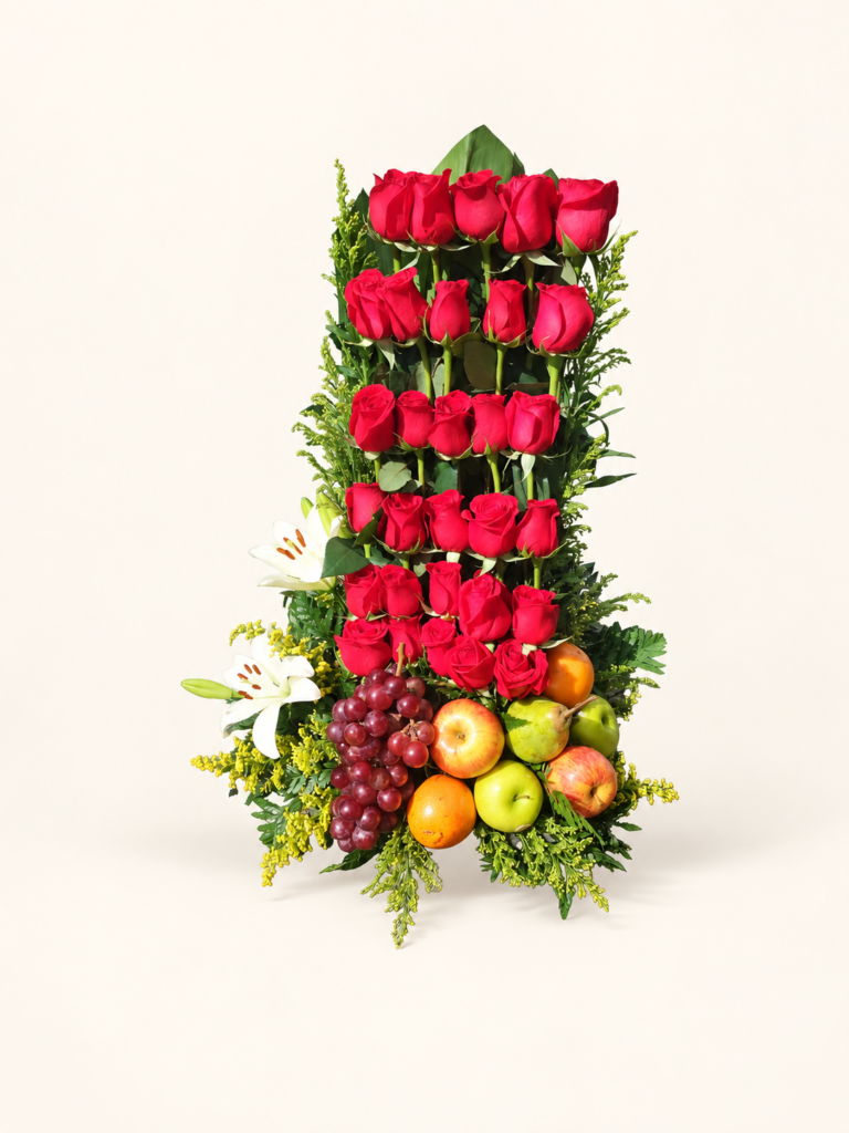Arreglo vertical de rosas rojas con lirios blancos, frutas y follaje decorativo. Sobre fondo crema.
