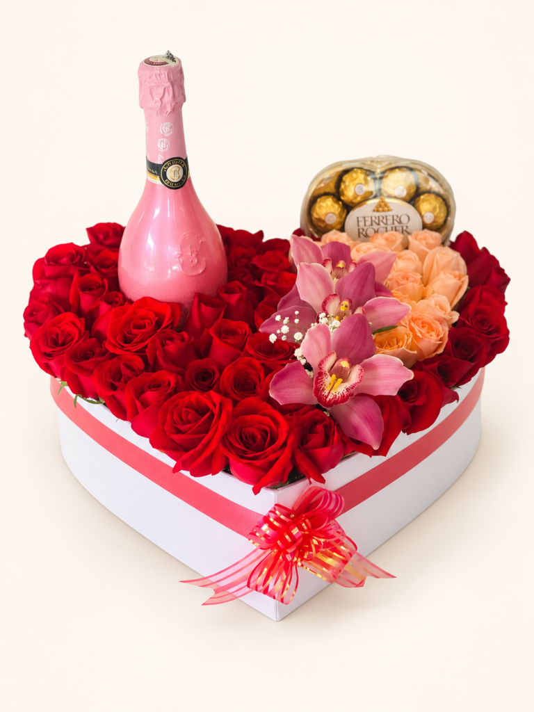 Corazón de rosas rojas y salmón con orquídeas rosadas, botella rosada y chocolates Ferrero Rocher. Sobre fondo crema.