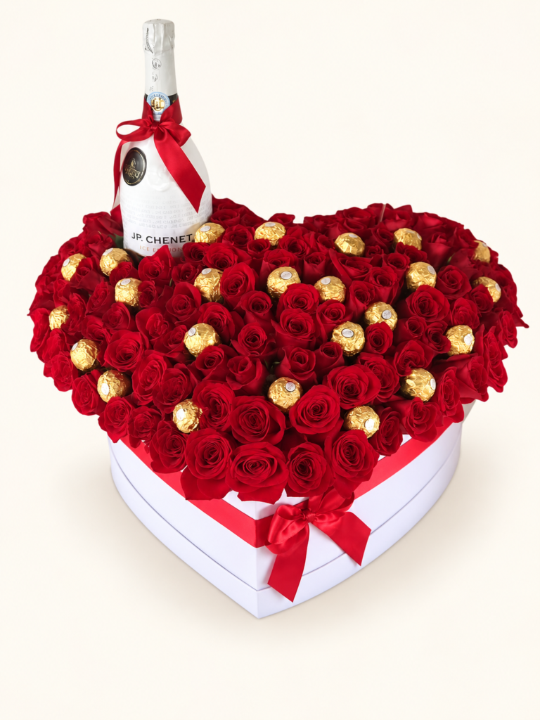 Caja corazón con rosas rojas, botella JP. Chenet y chocolates Ferrero Rocher entre las flores. Sobre fondo crema.