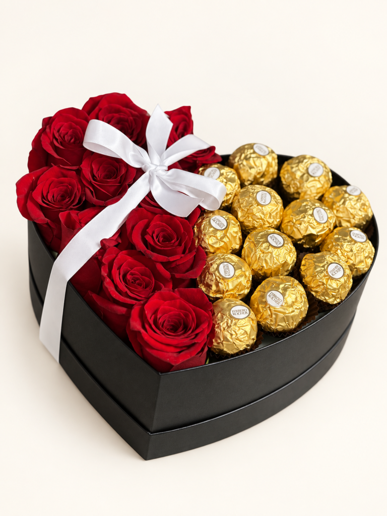 Caja negra en forma de corazón con rosas rojas, chocolates Ferrero Rocher y lazo blanco. Sobre fondo crema.