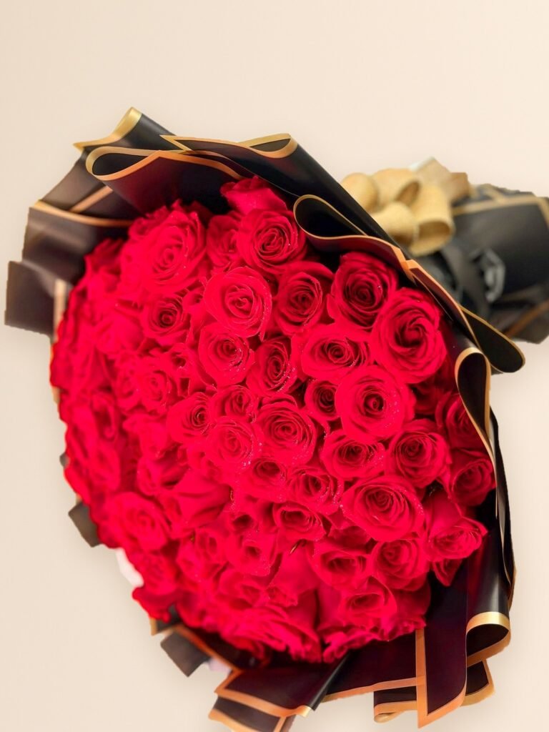 Ramo buchón de 100 rosas rojas con papel negro y borde dorado en Manizales sobre fondo crema