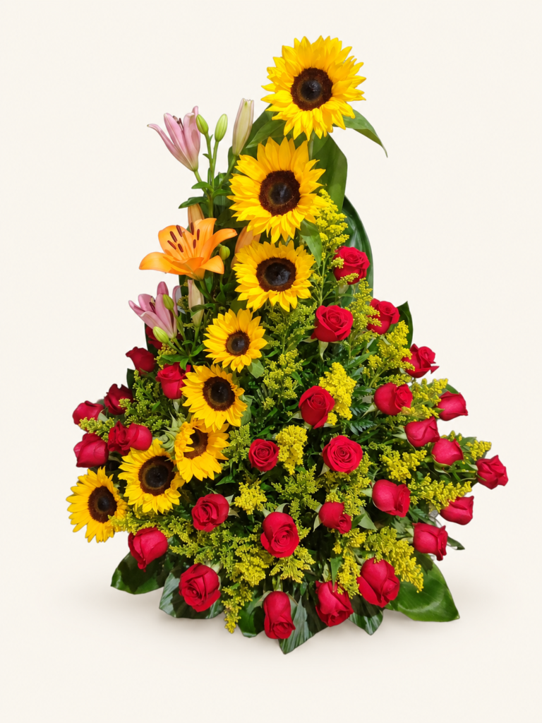 Arreglo de girasoles en cascada con rosas rojas, lirios y follaje. Sobre fondo crema.